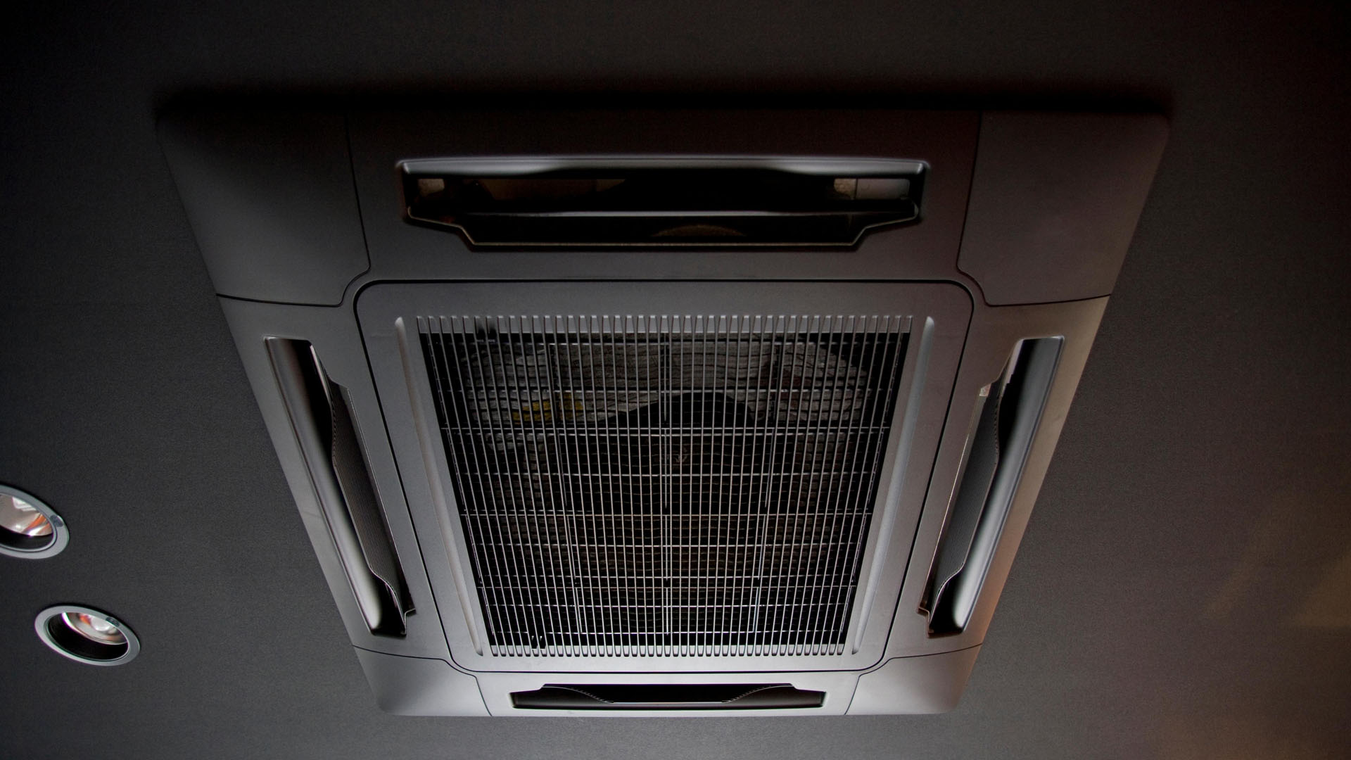 Sufitowy system klimatyzacji w pojeździe z centralną kratką wentylacyjną i bocznymi nawiewami.