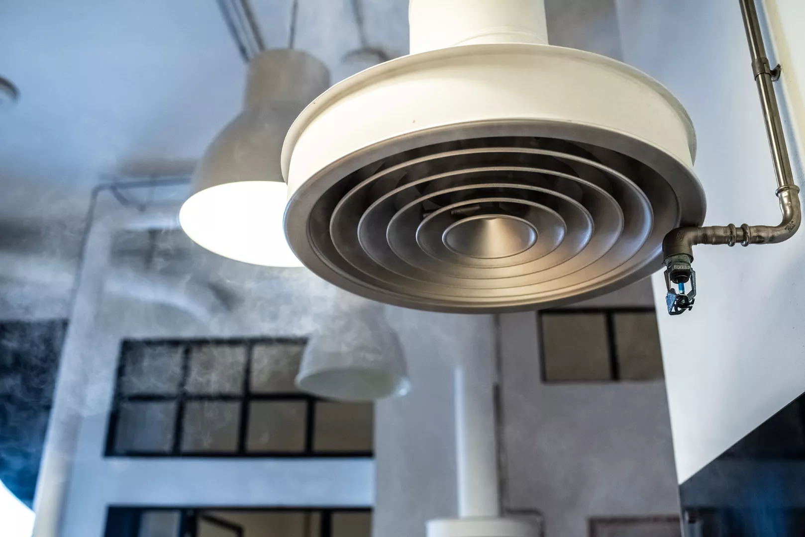 Duża okrągła centrala wentylacyjno-klimatyzacyjna zawieszona pod sufitem w surowym, przemysłowym wnętrzu.